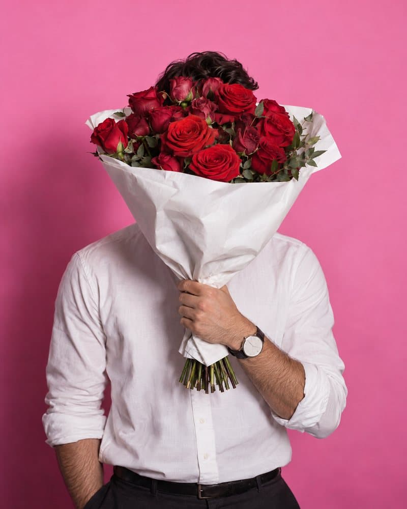 Man in a white shirt holding red roses in front of his face