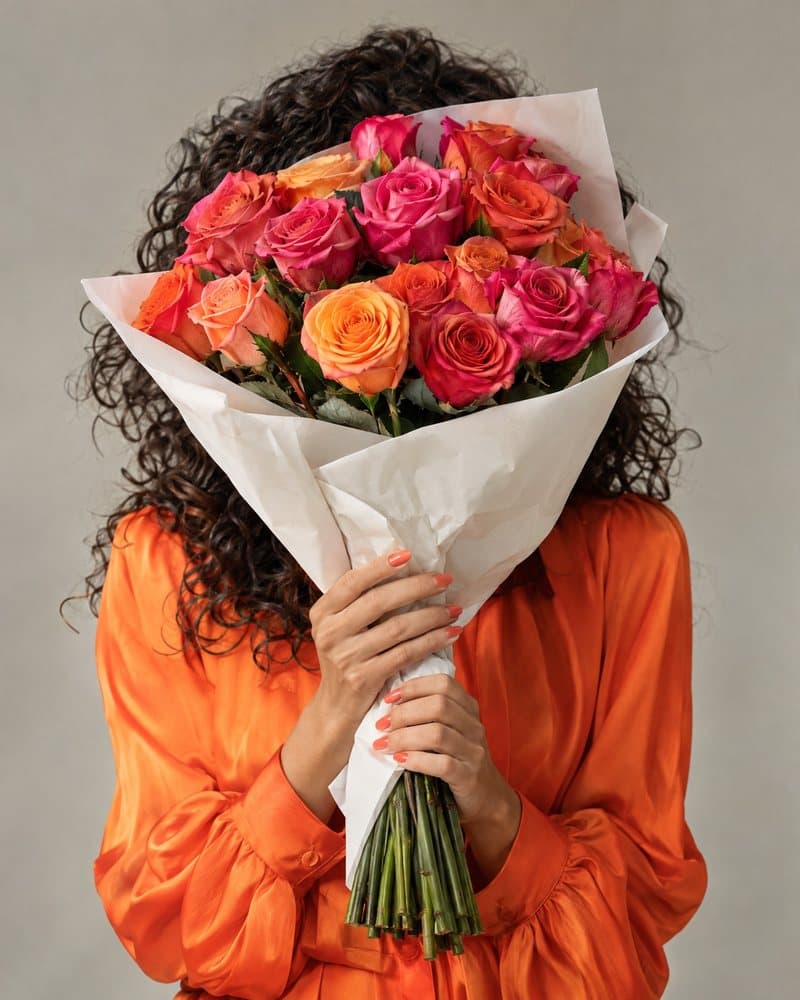 Woman in orange holding pink and orange roses in front of her face