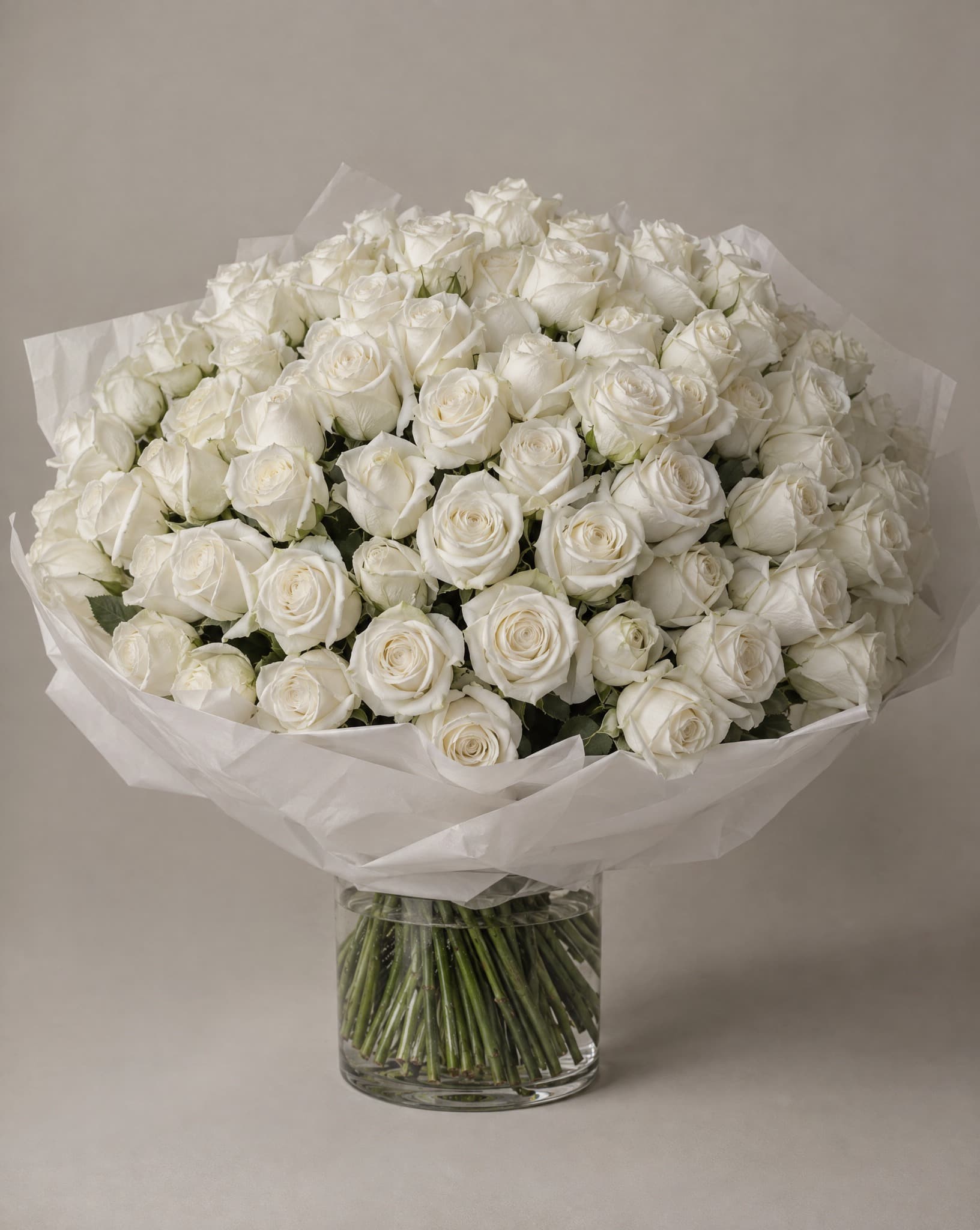 Pure white roses wrapped in white tissue in a clear glass vase