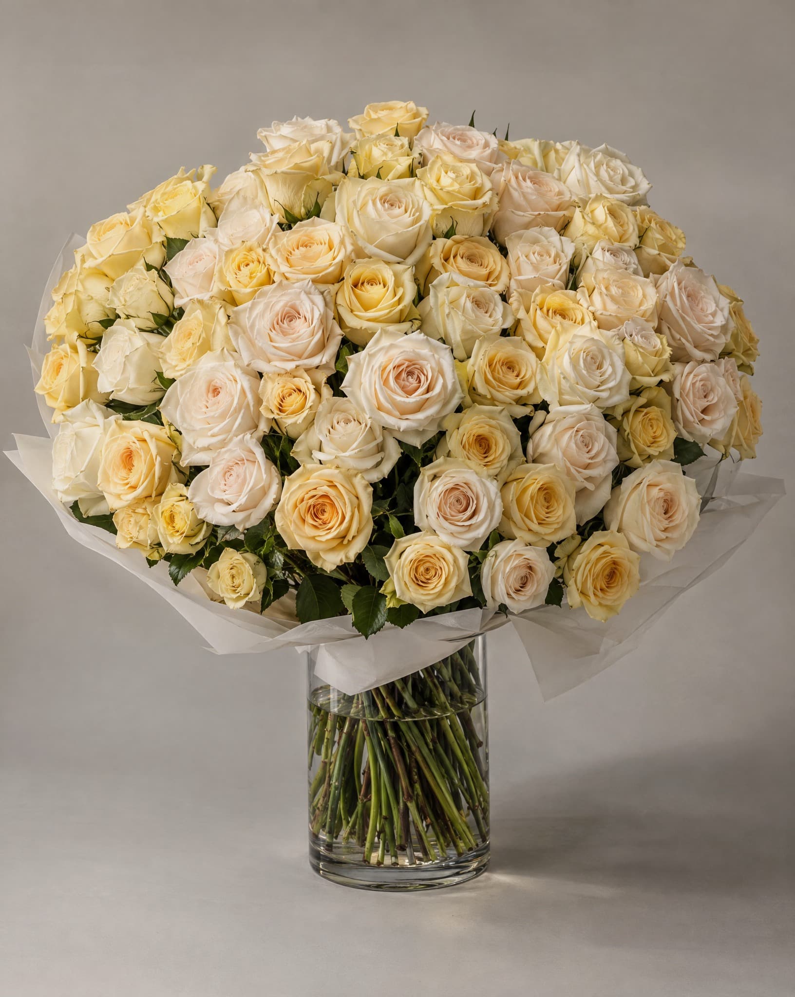 Cream and yellow roses wrapped in white tissue in a clear glass vase