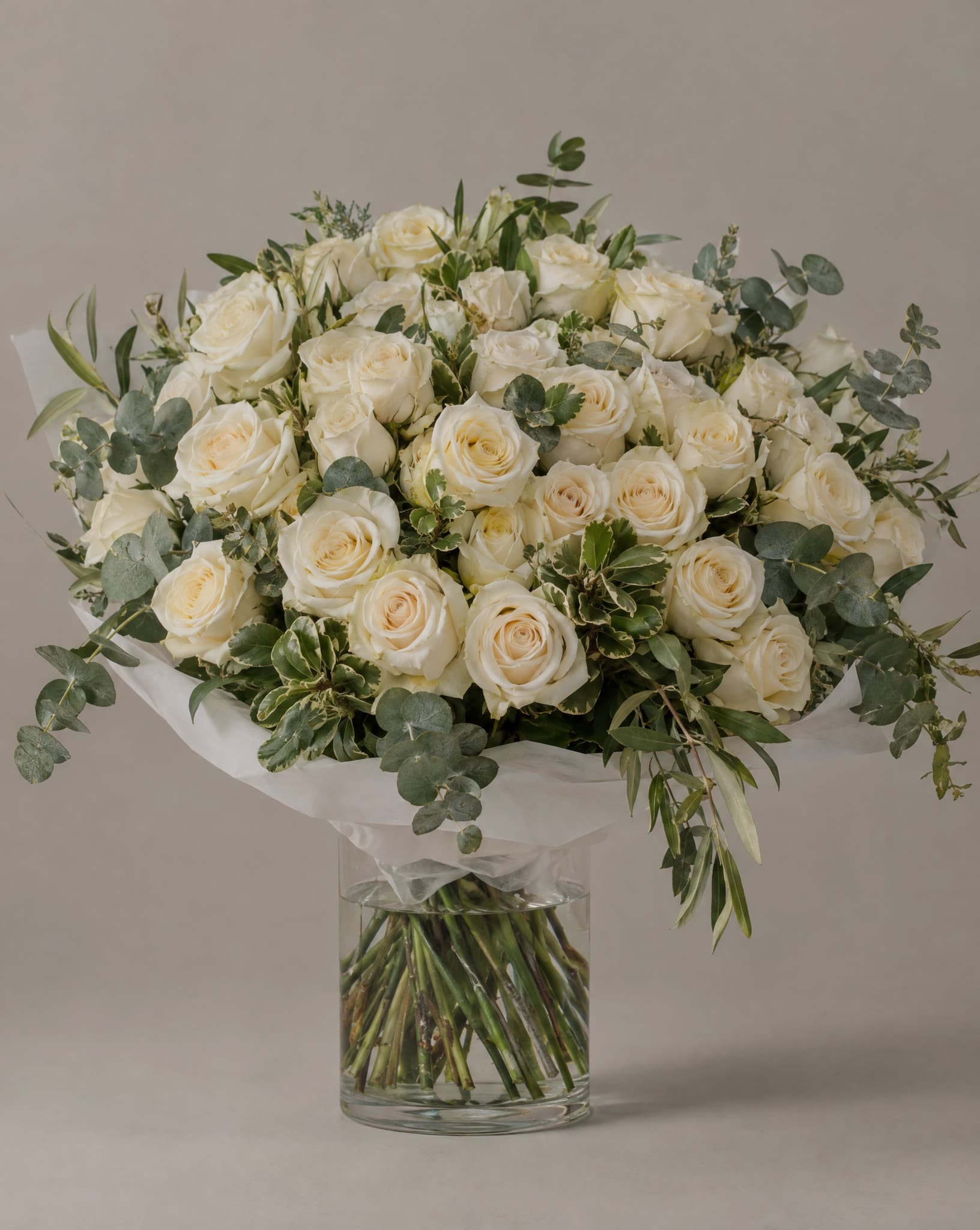 Cream roses with eucalyptus wrapped in white tissue in a clear glass vase