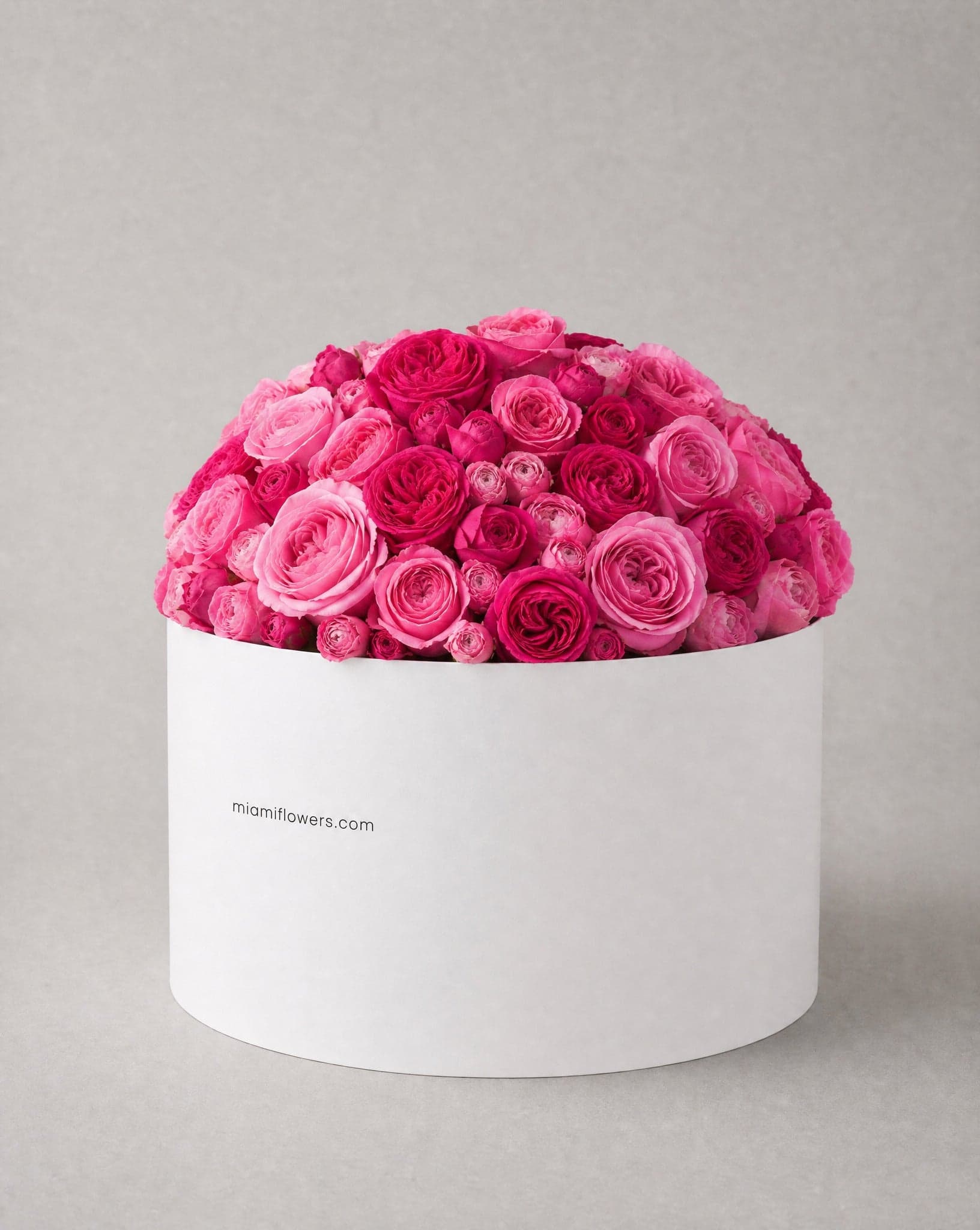 Bright pink and fuchsia roses in a tall matte white oval box printed with miamiflowers.com