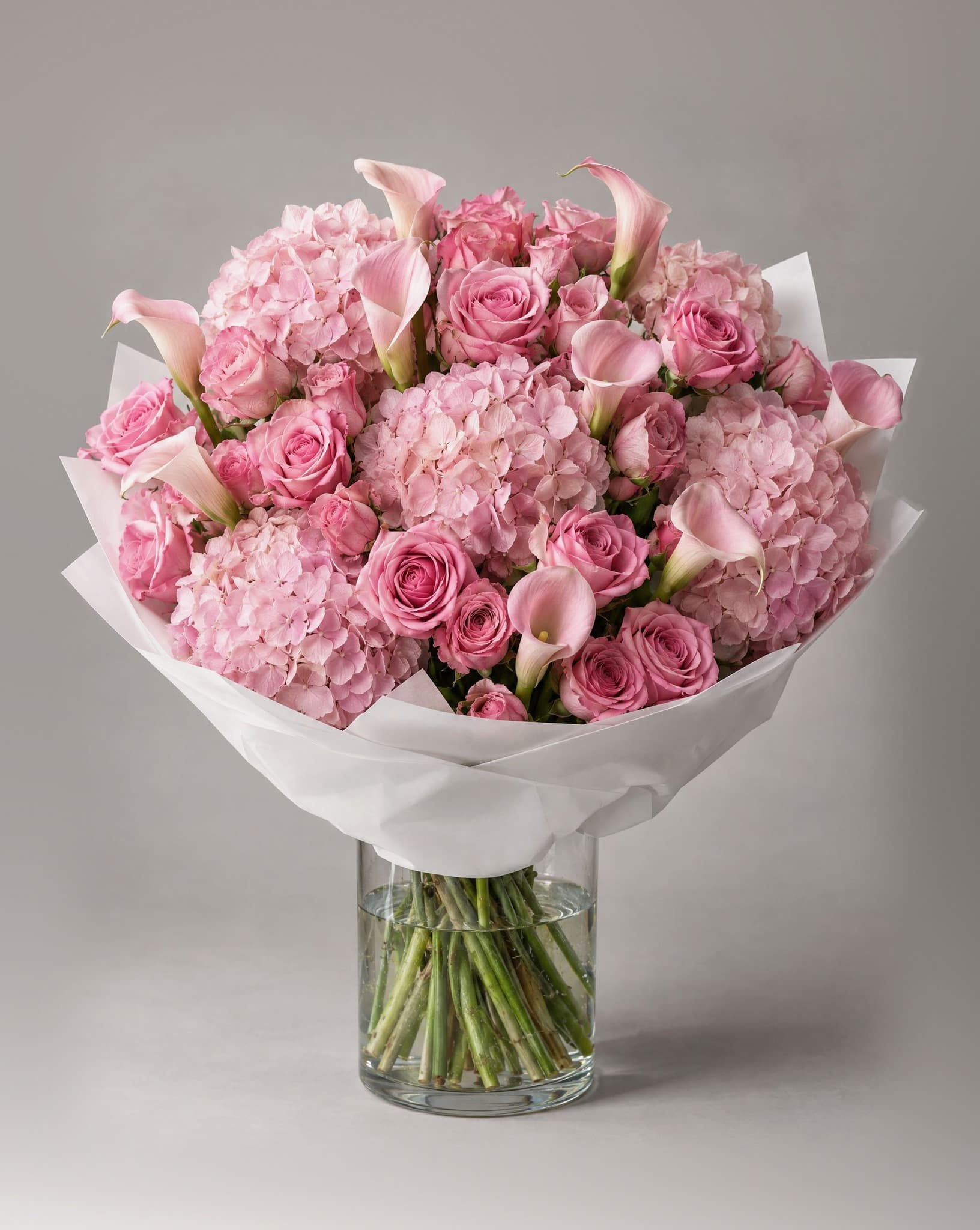 Grand bouquet of pink hydrangeas, pink roses and blush calla lilies in a clear glass vase